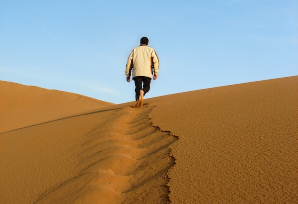 A man walks uphill in the desert sand