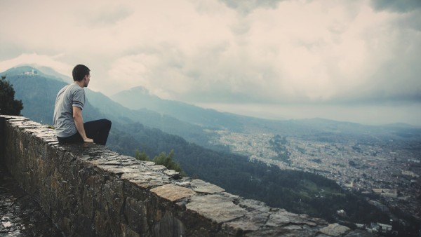 millennial man sitting on rock ledge