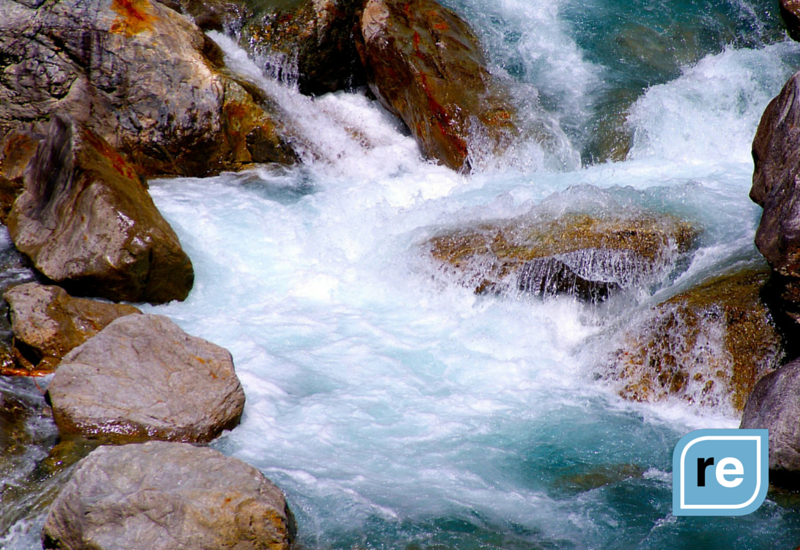 Rushing river waters cascade over rugged stones, embodying nature's relentless energy and dynamism.