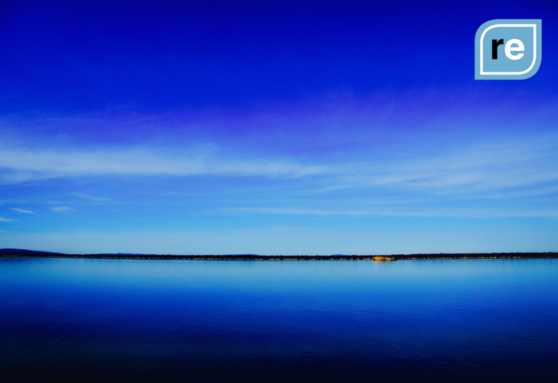 Serene lake under clear blue sky, horizon split by water's reflection, evoking tranquility and clarity.