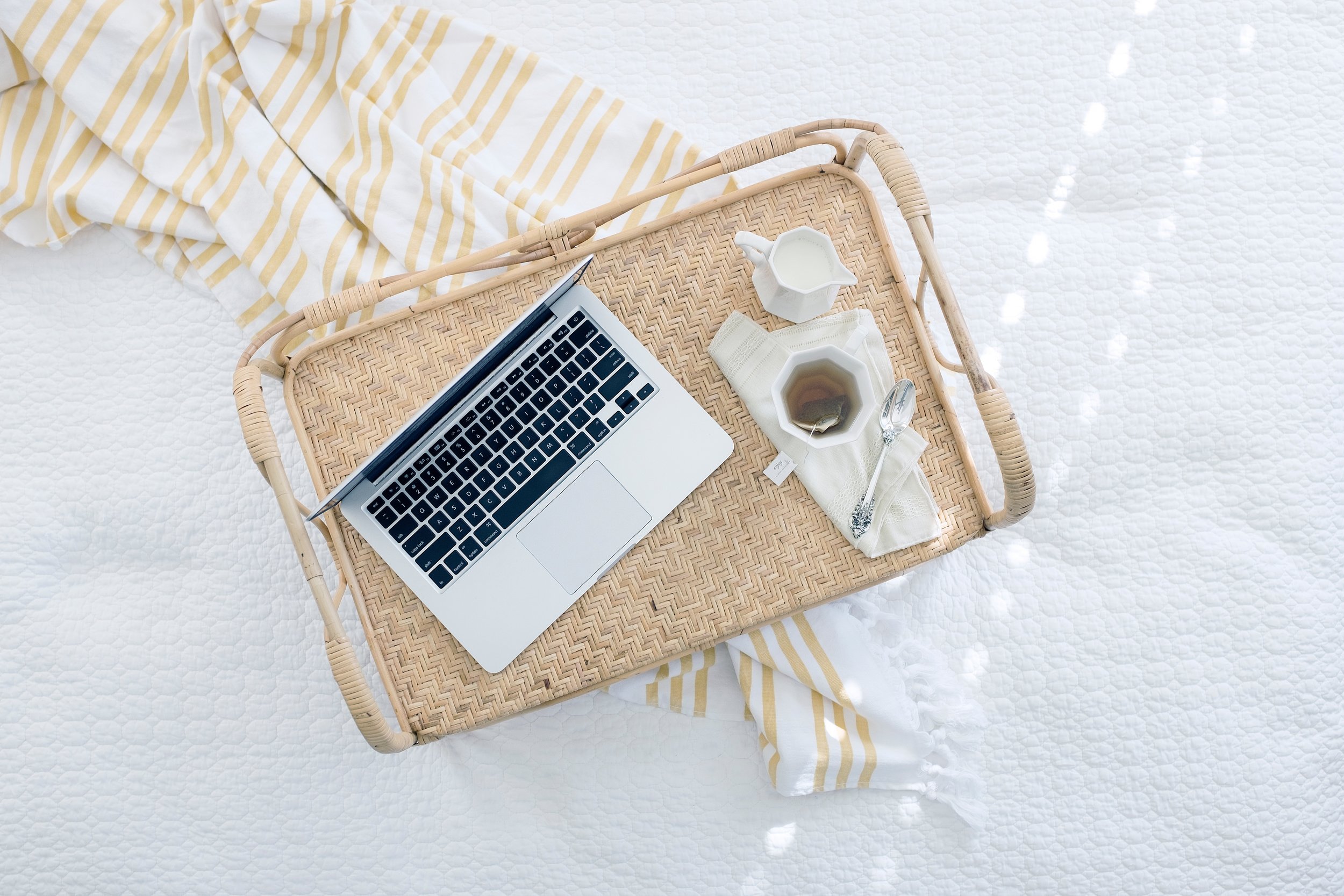 Laptop on woven tray with tea and napkin, casual remote work setup.