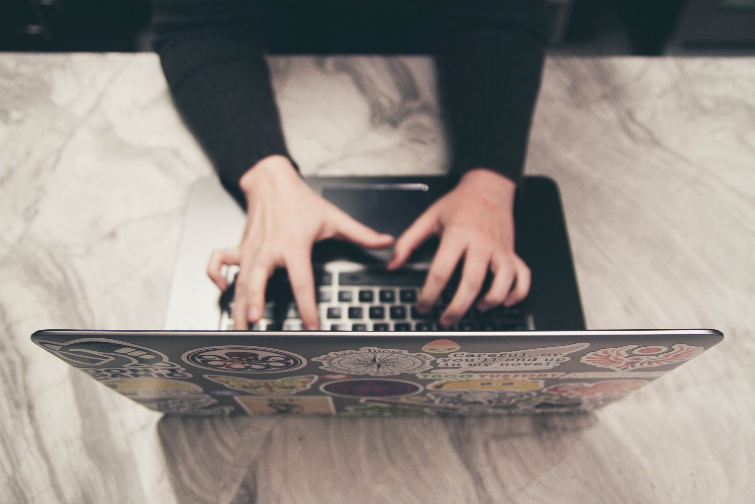 Close-up of hands typing on a laptop adorned with eclectic stickers, symbolizing casual digital communication