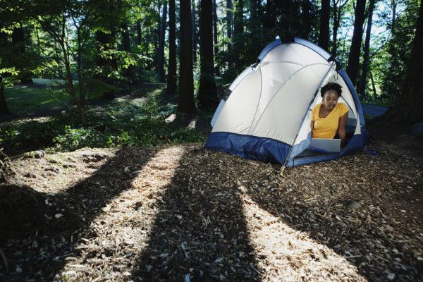 Person in a tent with a laptop, blending nature's tranquility with digital connectivity for AI-driven work.