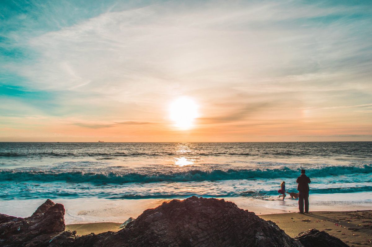 Sunrise over the ocean with a silhouette of a person and child, embodying the calm of AI-optimized life balance strategies.